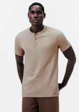 Remera de manga corta color beige, con cuello redondo y cartera con tres botones frontales.