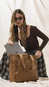 Cartera tipo tote marrón de diseño práctico y versátil, confeccionada en símil cuero con textura granulada. Cuenta con asas cortas fijas, bolsillos exteriores con cierre al frente y atrás, y bolsillos laterales abiertos. Su interior es amplio e incluye bolsillos organizadores. Viene con una correa ajustable y desmontable.