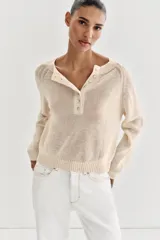 Jersey de punto color beige, con cuello redondo y cierre frontal parcial de botones, manga larga y acabados en rib.