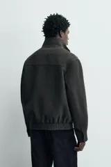 Cazadora de paño en color gris oscuro, con corte regular fit, cuello subido y cierre frontal de cremallera. Presenta bolsillos de vivo en la cadera, puños con botón y bajo elástico.