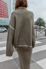 Jersey de punto con cuello subido y manga larga, de corte holgado. Presenta detalles de vivos en color crema en el cuello, puños y costuras de las mangas, contrastando con el tono marrón jaspeado de la prenda.