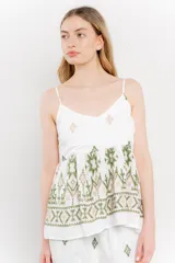 Blusa blanca de algodón liviano con tirantes finos y escote en V. Presenta un corte suelto con pechera fruncida y bordados artesanales en tonos verde y beige con motivos geométricos y florales.