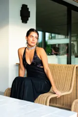 Vestido largo con estampado tie-dye en tonos violeta y fucsia, escote en V con detalles bordados dorados, cut-outs laterales bajo el busto y tirantes finos que se cruzan y atan en la espalda.