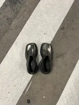 Zapato tipo mocasín color peltre con detalle de costuras en contraste y suela track color negro.