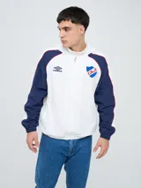 Campera deportiva Umbro del Club Nacional de Football, modelo Venti, para hombre. Diseño en color blanco con mangas azules y detalles de líneas rojas. Cuenta con capucha con cordón ajustable, cierre frontal y bolsillos. Presenta el logo de Umbro y el escudo del club bordados en el pecho.