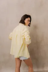 Camisa blanca de calce amplio, confeccionada en tejido liviano con sutiles rayas verticales, cuello clásico, mangas largas con hombros caídos y abotonadura frontal.
