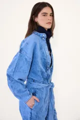 Mameluco de jean con efecto nevado estilo vintage, de corte holgado, mangas largas, cierre frontal con botones a presión y lazo ajustable en la cintura.