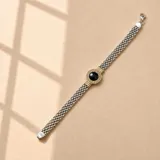 Pulsera de plata y oro de 18k con eslabones entrelazados y un dije central circular con detalles dorados y una piedra de ónix negro.