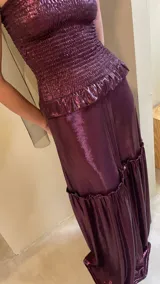 Vestido largo strapless de lamé elastizado color bordó, con cuerpo fruncido tipo corsel y falda larga amplia con volados y frunces.