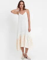 Vestido largo vaporoso de ramio, de color blanco, con tirantes finos, escote en V y un impresionante bordado en el bajo. Silueta fluida.