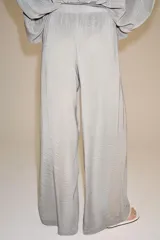 Pantalón palazzo gris de tejido semitransparente con tiro medio, cintura elástica, bolsillos laterales y forro interior corto.