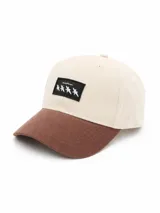 Gorra de béisbol bicolor con corona en color beige y visera marrón. Cuenta con un parche rectangular negro en el frente con cuatro estrellas blancas y texto bordado.