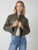 Chaqueta corta de eco cuero color tostado, con cuello alto, cierre frontal con botones a presión y bolsillos de solapa en el pecho. Tiene forro interno a tono.