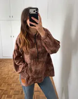 Canguro con capucha y cordones ajustables, de diseño holgado con mangas abullonadas y puños elásticos. Presenta un estampado animal print en tonos marrones y un bolsillo frontal tipo canguro con etiqueta de cuero sintético.
