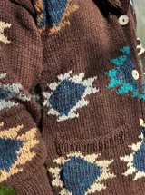 Saco de lana azul marino con diseño geométrico en tonos beige, rojo y gris. Tiene cuello esmoquin, cierre con botones y bolsillos delanteros.