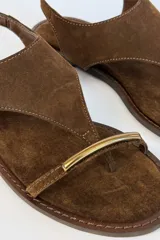 Sandalia plana de gamuza color tostado, con diseño de tira en T y argolla metálica en el empeine. Cuenta con tira ajustable con hebilla en el talón.