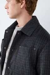 Campera de paño con diseño a cuadros, cuello clásico, cierre frontal con botones metálicos y bolsillos frontales tipo parche.