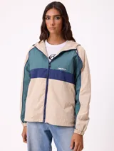 Campera rompevientos Rusty de diseño color block, con cierre frontal, capucha y puños elásticos. Presenta una combinación de tonos beige, verde azulado y azul marino, con el logo de la marca bordado en el pecho.