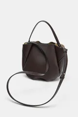 Bolso de mano tipo saco mini, color marrón oscuro, con detalle de pespuntes en el cuerpo y cierre mediante botón imantado. Incluye tira ajustable frontal y compartimento interior con cremallera.