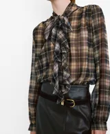 Blusa de manga larga con estampado de cuadros en tonos marrones y grises, cuello clásico y cierre frontal con botones ocultos.