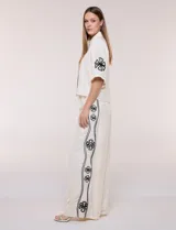 Conjunto de dos piezas negro compuesto por camisa de manga corta con cuello camisero y pantalón palazzo de tiro alto. Presenta detalles de bordados florales en contraste a lo largo de los laterales del pantalón y en las mangas.