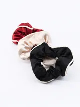 Set de tres scrunchies (coleteros) de tela satinada, uno rojo oscuro, uno beige claro y uno negro. Todos tienen un borde exterior de cordón trenzado color crudo.