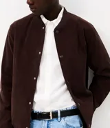 Campera bomber masculina de terciopelo cotelé color beige, con cuello redondo, mangas largas, cierre frontal de botones forrados, bolsillos laterales y terminaciones de elástico en puños y cintura.