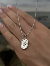 Collar plateado con cadena fina y dije ovalado con relieve de una rosa.