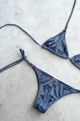 Conjunto de bikini con corpiño triangular de atar con apliques de argollitas y bombacha vedetina de atar con apliques de argollitas. El tejido presenta un estampado tie-dye o marmolado en tonos lila/azul y naranja/beige.