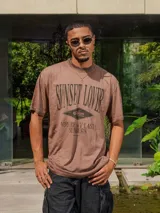 Remera de jersey con efecto teñido, color marrón, de corte holgado y cuello redondo. Presenta un estampado frontal con texto en tonos más oscuros.