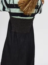 Vestido midi de denim color marrón, con corte holgado, breteles finos con lazos ajustables y detalle de volado en el ruedo.