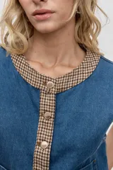 Chaleco de denim azul con detalles de ribetes en estampado de pata de gallo en tonos marrones. Presenta cierre frontal con botones metálicos y un bolsillo de parche en el frente.