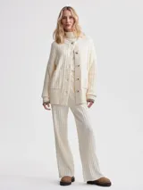 Cárdigan largo color crema, confeccionado en tejido de punto acanalado de viscosa. Tiene corte relajado, cierre frontal con botones y bolsillos de parche.