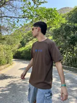 Remera marrón con estampa azul de flores y texto "Abundance is a mindset".