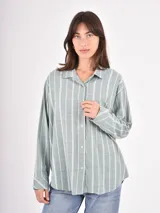Camisa de corte holgado con estampado de rayas verticales en tonos verde y blanco, cuello clásico, cierre frontal con botones y bolsillo en el pecho.