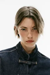 Cazadora de denim azul oscuro, de corte entallado, cuello redondo y manga larga. Cuenta con cierre frontal con alamares y costuras pespunteadas en contraste.