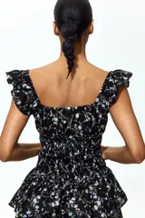 Vestido corto negro con estampado floreado, escote cuadrado con volados en los tirantes, cuerpo fruncido tipo nido de abeja y falda de capas escalonadas.
