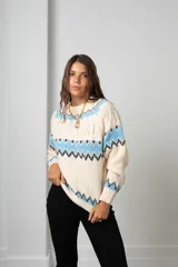 Buzo de tejido de punto con diseño nórdico, cuello redondo acanalado y mangas largas. Presenta un patrón geométrico en tonos celeste, negro y crema.