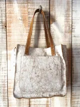 Bolso tote de cuero con acabado craquelado en tonos blanco y marrón claro. Posee asas de mano y tiras de hombro de cuero marrón liso. Cuenta con un bolsillo exterior frontal grande.