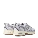 Championes New Balance modelo 530, con diseño retro-deportivo. Presentan una capellada de malla blanca transpirable con refuerzos sintéticos en tonos gris claro y lila. Incorporan entresuela con tecnología ABZORB para amortiguación y suela de goma en color marrón.