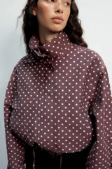 Cazadora negra con estampado de lunares blancos, cuello subido, manga larga, bolsillos delanteros, bajo ajustable con cordones y cierre frontal con cremallera y solapa con botones ocultos.