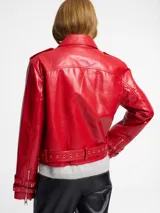 Chaqueta biker negra de cuero sintético con tachas plateadas en los hombros y solapas, cierre asimétrico con cremallera, cinturón ajustable con hebilla y detalles metálicos.