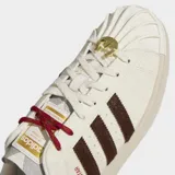 Championes Adidas Superstar II con exterior de cuero y material sintético en color blanco crema. Presentan las icónicas tres tiras laterales y refuerzo en el talón en color marrón oscuro texturizado, puntera de goma con relieve y suela de caucho al tono.