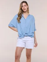 Blusa estilo denim de lyocell celeste, de silueta amplia y suelta, con escote en V, cartera frontal de botones y mangas cortas japonesas de hombros caídos. Cuenta con ruedo asimétrico y posibilidad de anudar al frente.