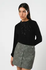 Minifalda gris con textura símil cuero, corte irregular con sobrefalda y cierre frontal con broches metálicos.