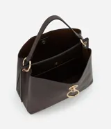 Bolso mediano color marrón oscuro, con doble asa corta y correa larga extraíble. Presenta textura símil cuero y detalle de aro dorado en el frente.