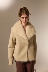 Chaqueta de eco-cuero color beige con interior y cuello de piel sintética al tono. Presenta un diseño holgado, cierre frontal con un botón y solapas amplias.