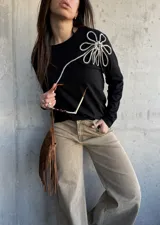 Remera de manga larga color negro, de corte recto, con aplique decorativo en relieve con forma de flor grande en el hombro confeccionado con cordón trenzado en blanco y negro.