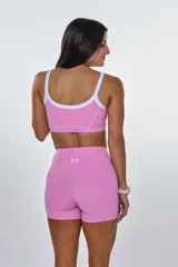 Conjunto deportivo compuesto por un top y un short de tiro alto en color rosa. El top presenta breteles finos blancos, escote redondo y el logo 'bk.' estampado en el centro. El short cuenta con costuras decorativas blancas que resaltan el diseño.