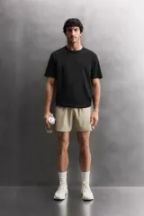 Pantalón corto deportivo color marrón oliva, confeccionado en tejido técnico ligero y elástico, con forro interior. Presenta cintura elástica ajustable con cordón, bolsillos frontales, bolsillo de seguridad trasero con cierre y aberturas laterales en el bajo.